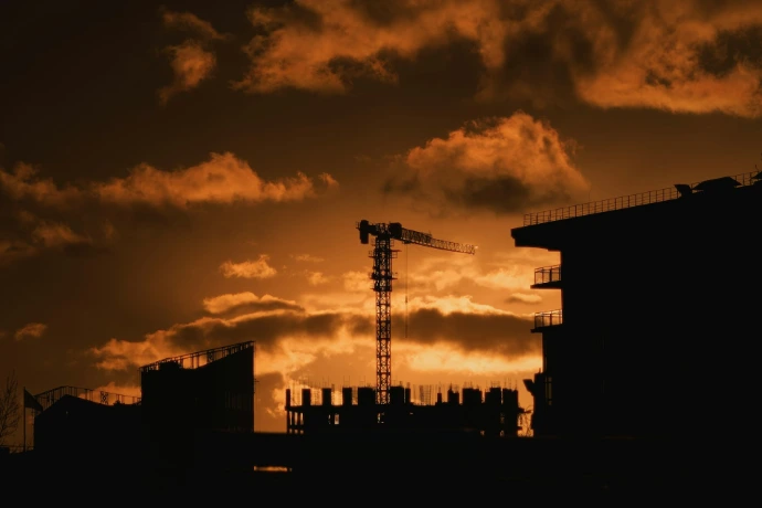 Construction crane silhouetted against a dramatic sunset sky.
